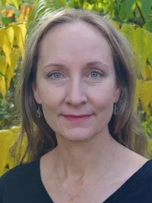 Smiling woman with blond hair in front of yellow and green leaves