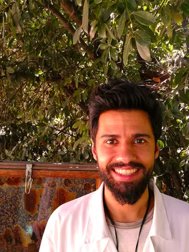 A smiling man with dark hair and beard in front of an observation beehive