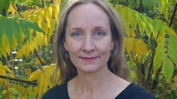 Smiling woman with blond hair in front of yellow and green leaves