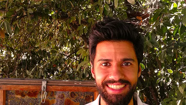 A smiling man with dark hair and beard in front of an observation beehive